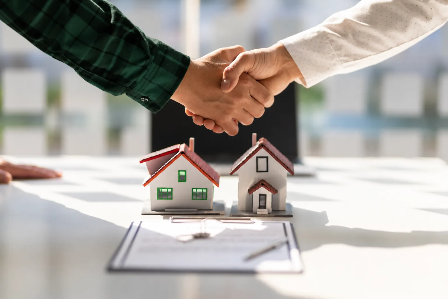 Aperto de mãos sobre uma mesa com maquetes de casas e um contrato